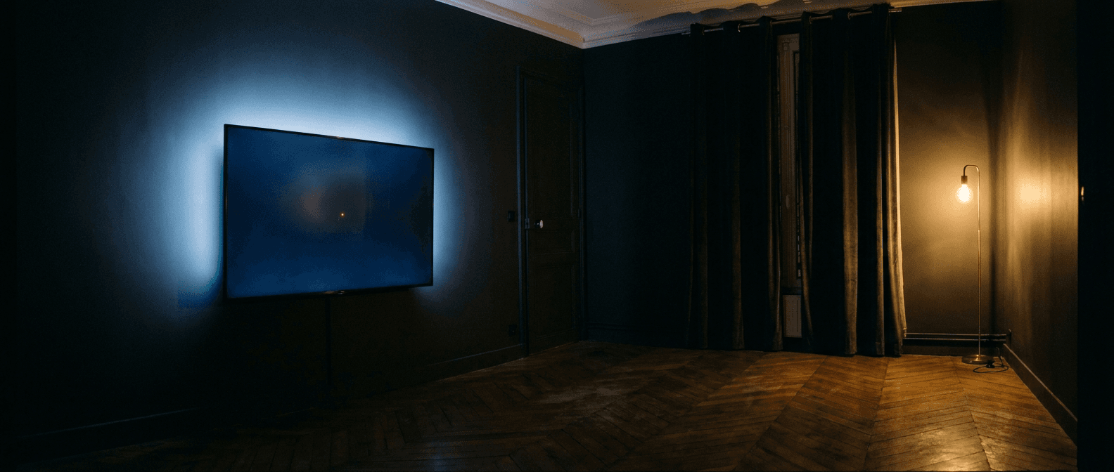 Salon français vide la nuit — TV murale émettant une lueur bleue.